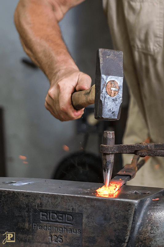 Schmied schlägt glühenden Stahl mit einem Hammer auf dem Amboss