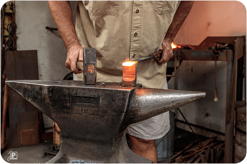 Blacksmith hitting steel on an anvil with a hammer